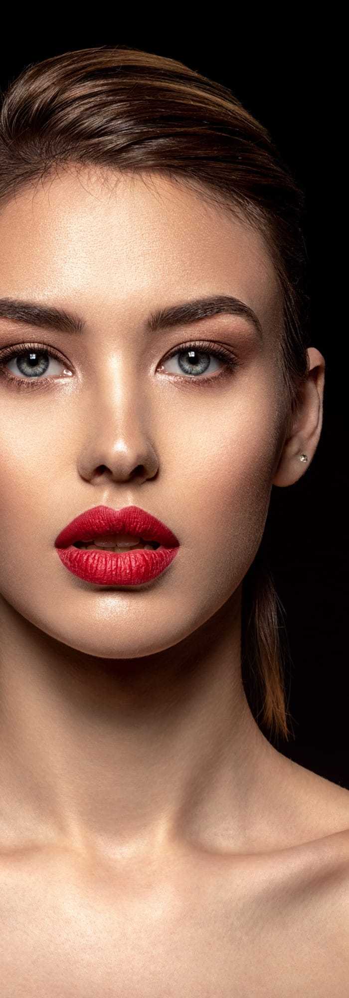 Close-up of a woman with striking makeup on a dark background.